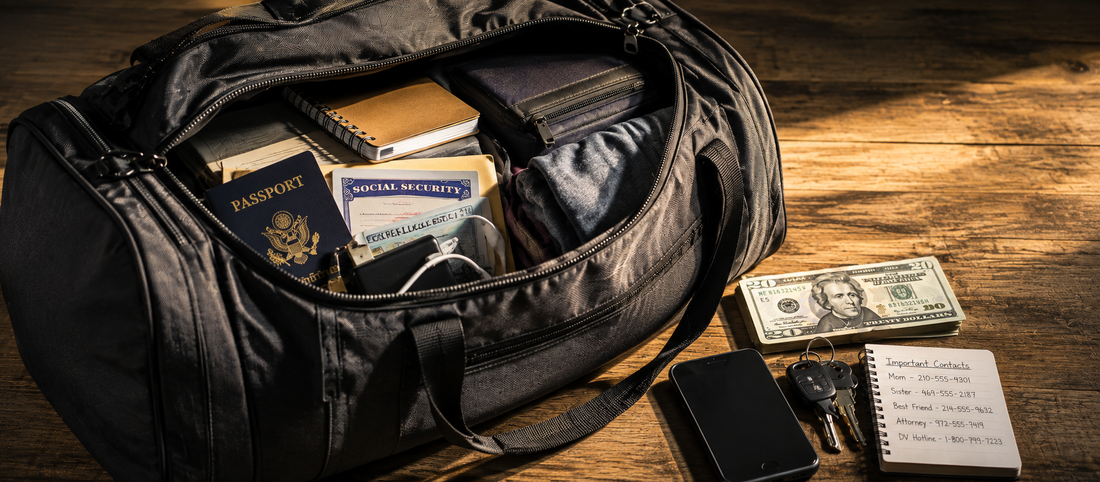 A prepared black duffel bag containing identification, documents, clothing, and essential items beside cash, keys, a phone, and written emergency contacts for safety planning.